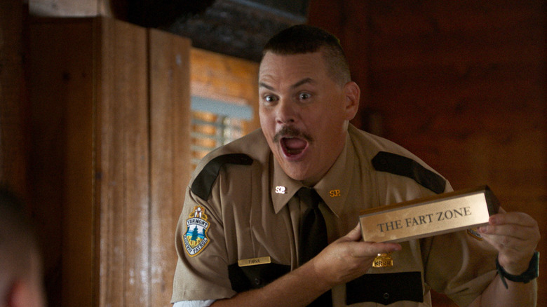 Kevin Heffernan as Farva holding up his Fart Zone nameplate in Super Troopers 2