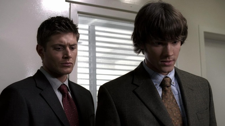 Jensen Ackles' Dean Winchester and Jared Padalecki's Sam Winchester, both wearing suits, speak to someone in season 1 of Supernatural