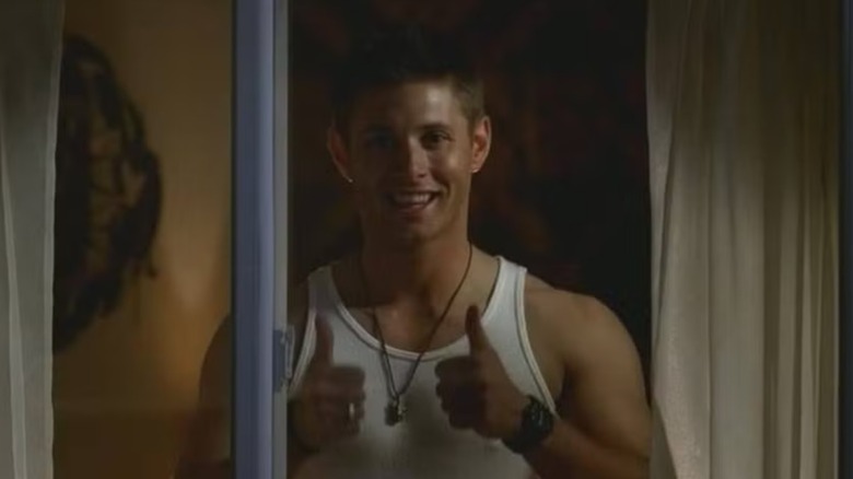 Jensen Ackles' Dean Winchester gives a double thumbs up from a motel window in Supernatural