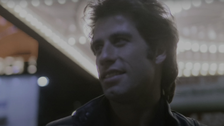 John Travolta's Tony Manero smiles as he walks under the bright lights of a marquee in Staying Alive