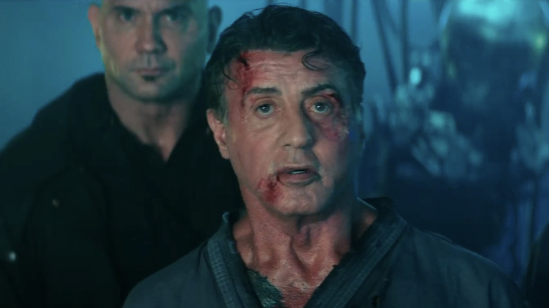 Sylvester Stallone's Ray Breslin stands bloodied in front of Dave Bautista's Trent DeRosa in Escape Plan 2