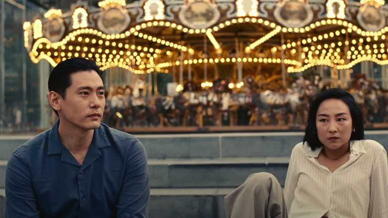 Hae Sung and Nora sitting in front of a carousel in Past Lives