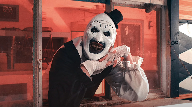 David Howard Thornton's Art the Clown rests his head on his hands while leaning through a serving hatch in Terrifier 2