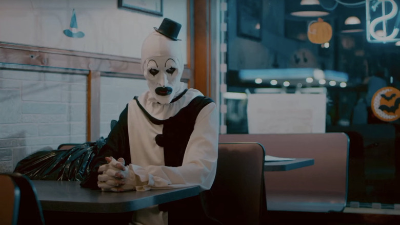 Art the Clown looks angry as he sits in a diner in Terrifier