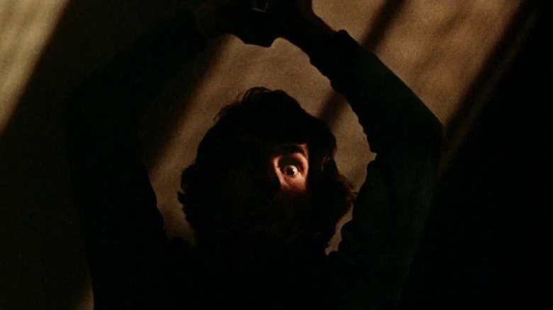 Billy obscured by shadows holding up a shard of glass in "Black Christmas" (1974)