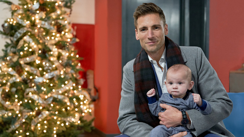 Luke posing with baby by Christmas tree in Three Wise Men and a Baby