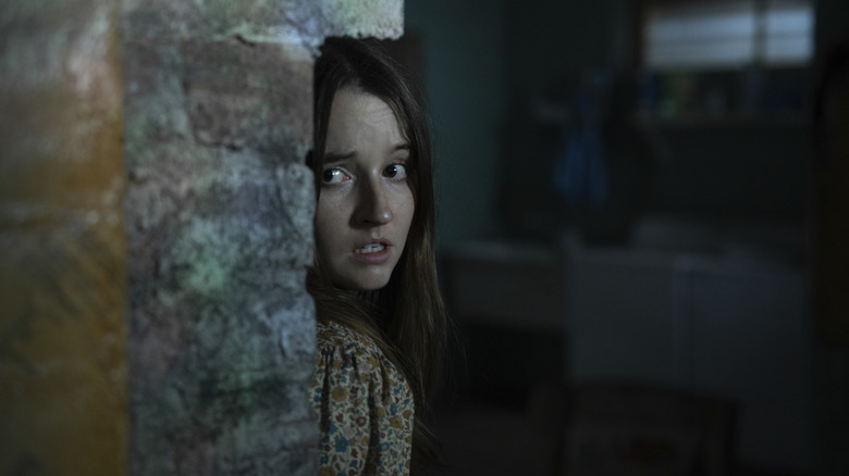 Kaitlyn Dever as Brynn in No One Will Save You hiding behind a brick wall