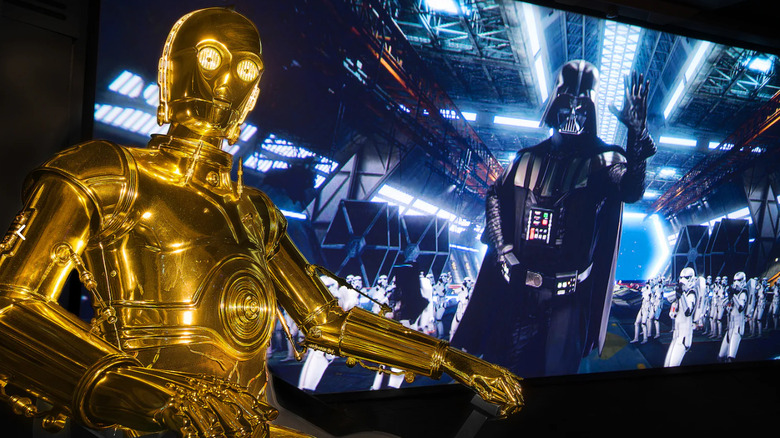 C-3PO sitting in front of a screen featuring Darth Vader