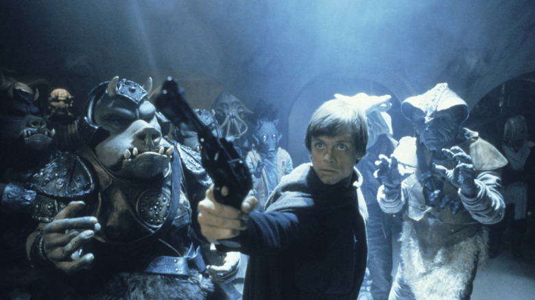 Mark Hamill as Luke Skywalker, pointing a blaster upwards and surrounded by fierce-looking alien guards in Star Wars: Return of the Jedi