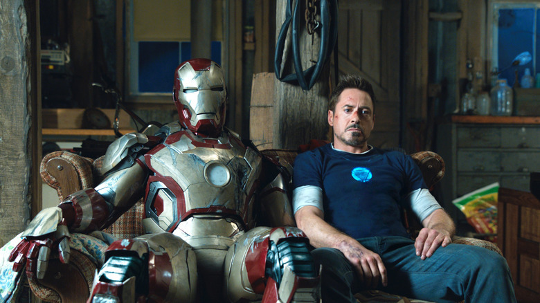 The Iron Man suit and Tony Stark sitting next to each other on a couch, looking tired in Iron Man 3