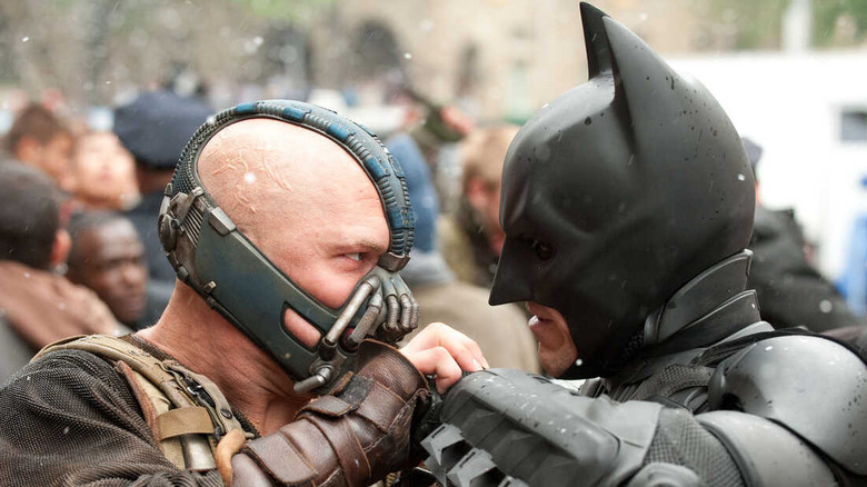 Tom Hardy as the supervillain Bane and Christian Bale as Batman, with Bane gripping onto Batman's left fist in a fight in The Dark Knight Rises