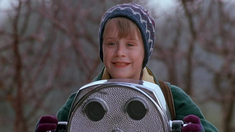 Macaulay Culkin's Kevin smiles while standing by a tourist binocular stand in Home Alone 2