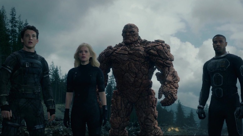 Miles Teller as Reed Richards, Kate Mara as Sue Storm, Jamie Bell as the Thing, and Michael B. Jordan as Johnny Storm all standing together in cratered, wooded area in Fantastic Four 2015