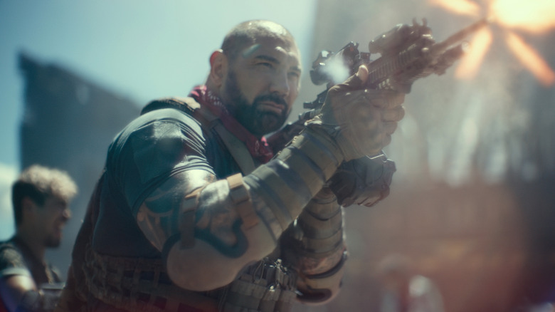 Dave Bautista raises a sniper rifle.