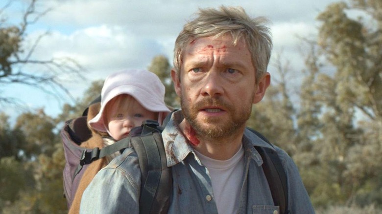 Martin Freeman with a baby strapped to his back.