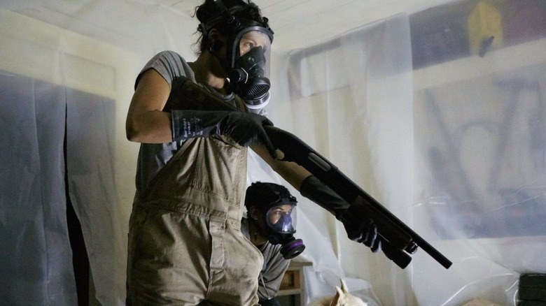 A woman wearing a gas mask raises a shotgun.