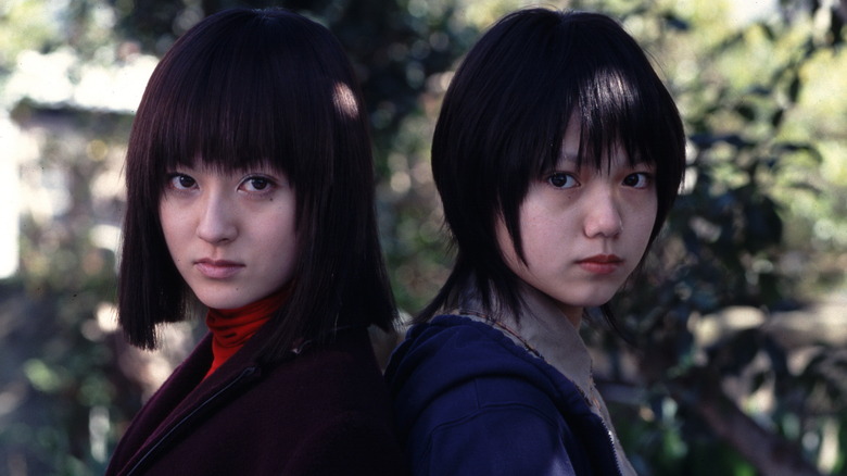 Two young women stand back to back, looking at the camera