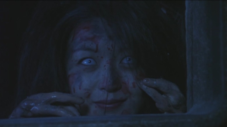 A woman looks through a window, covered in blood and smiling