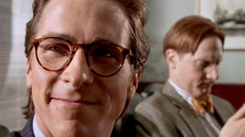 Christian Bale as Patrick Bateman smiling and wearing glasses in American Psycho