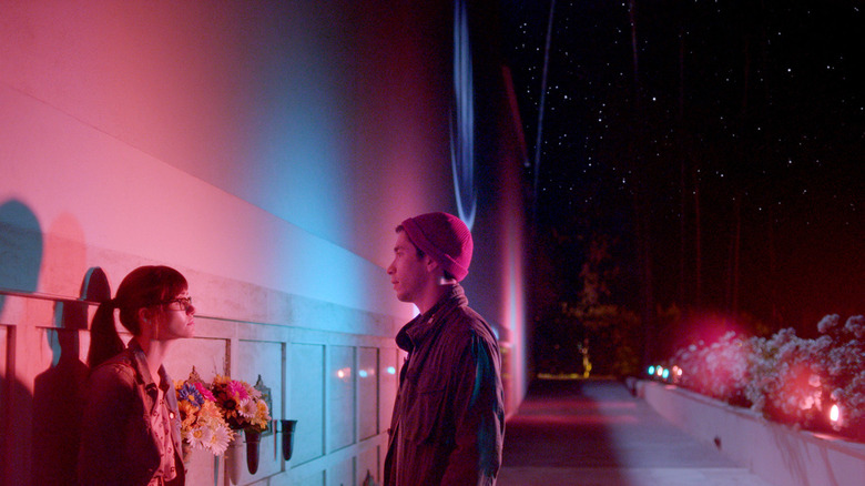 Dell speaks with Kimberly next to a neon-lit building in Comet