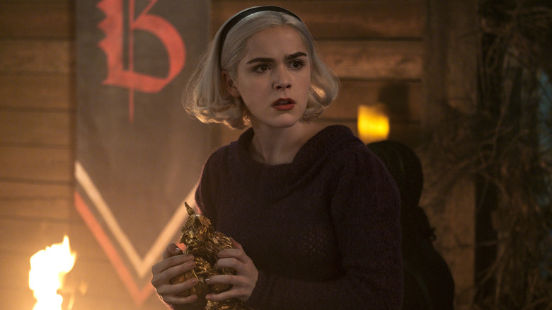 Kiernan Shipka as Sabrina Spellman holding a small statue in Chilling Adventures of Sabrina