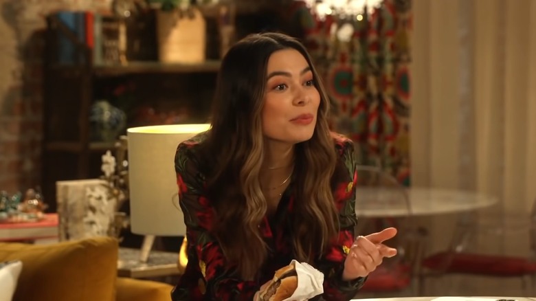 Miranda Cosgrove as Carly Shay holding a burger and speaking in iCarly (2021)