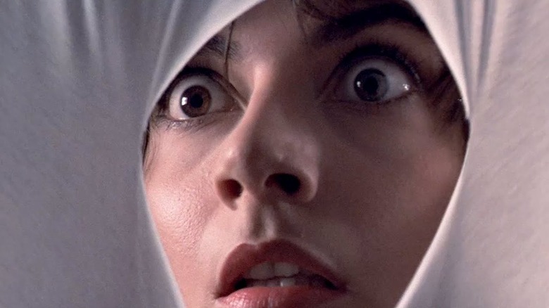 A woman looks throw a hole in white fabric in Tenebrae