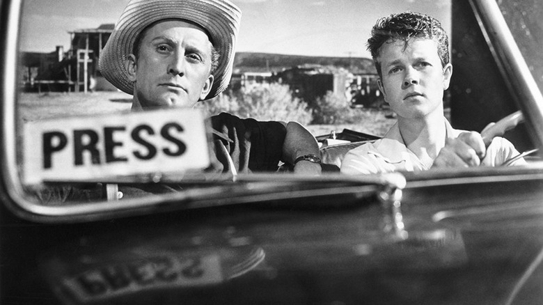 Two men in a convertible with a Press Pass on the windscreen