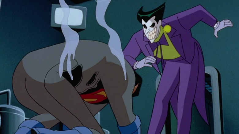 Joker prances above a smoldering Superman