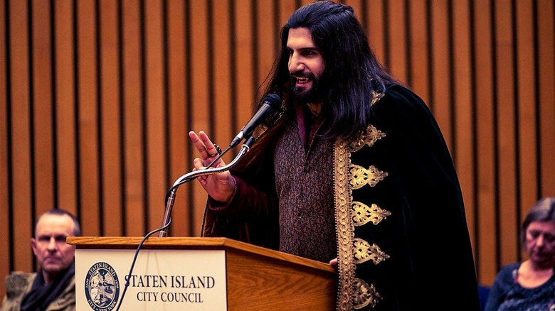 Nandor stands at a podium, delivering a speech