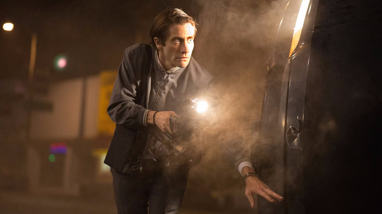 Lou Bloom holding a flashlight and handheld camera while sneaking around a van in Nightcrawler