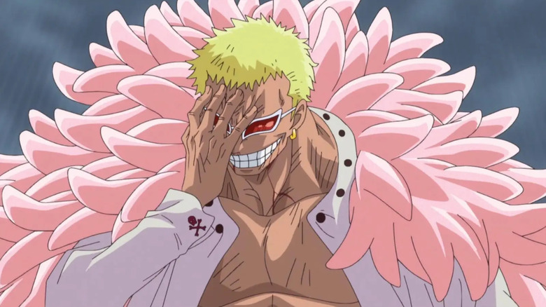 Donquixote Doflamingo touches his face as he laughs in One Piece