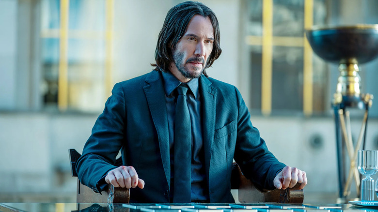 Keanu Reeves as John Wick, sitting at an outdoor table in John Wick: Chapter 4