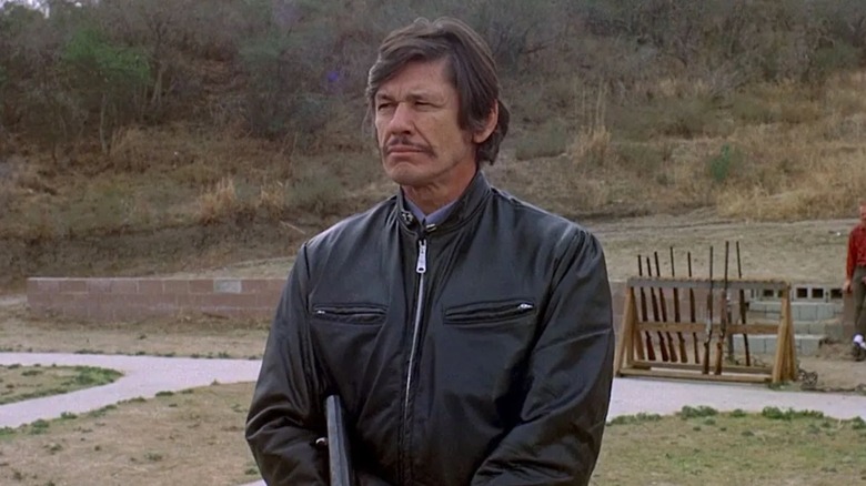 Charles Bronson as Arthur Bishop holding a gun outdoors in The Mechanic (1972)