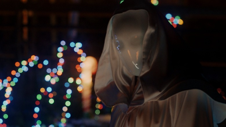 White masked figure in front of Christmas lights