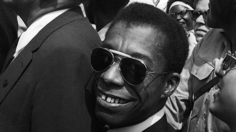 James Baldwin wears sunglasses and smiles