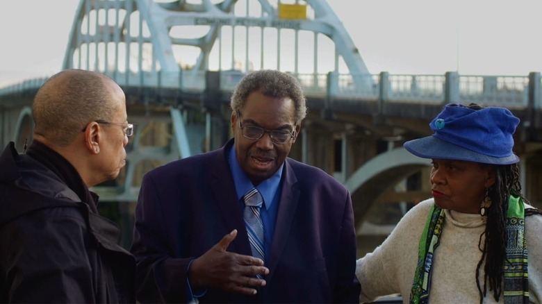 Three Black people talk in front of Edmund Pettus bridge