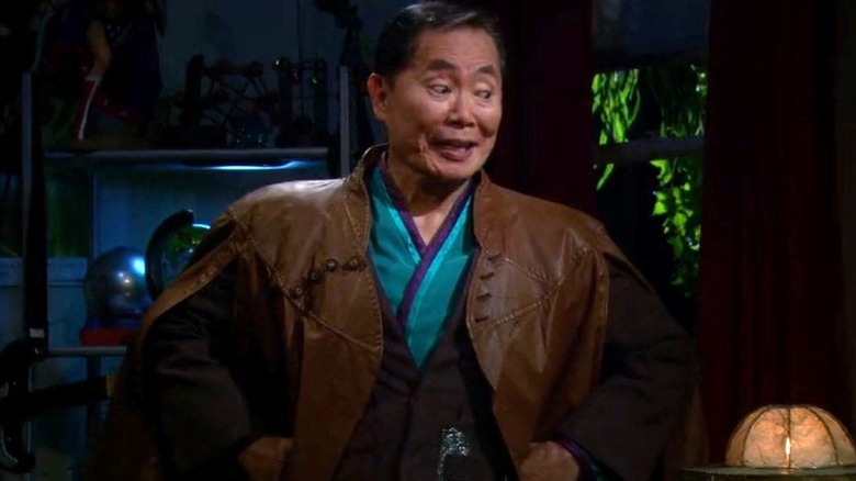 George Takei as himself stands in Howard's bedroom and looks toward the right with his hands on his hips while wearing a brown, blue, and purple outfit on The Big Bang Theory