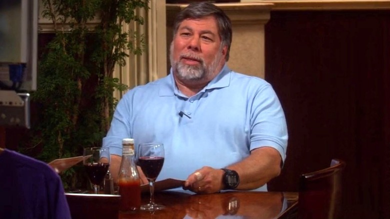 Steve Wozniak as himself sits at a table while talking to a robotic version of Sheldon Cooper played by Jim Parsons on The Big Bang Theory