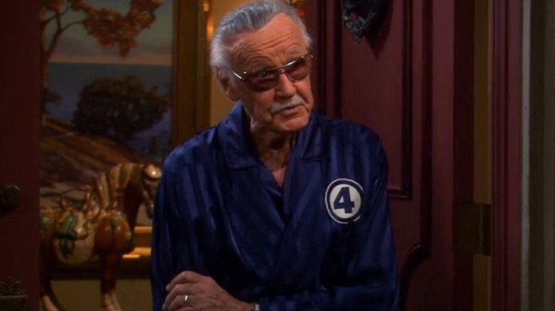 Stan Lee as himself stands in the doorway of his home while wearing a blue striped robe that has The Fantastic Four logo on the right side as he looks toward the right on The Big Bang Theory