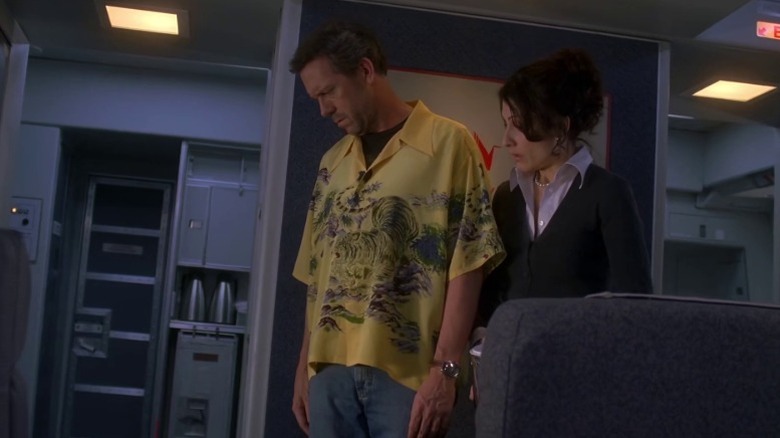 Hugh Laurie as Dr. Gregory House and Lisa Edelstein as Dr. Lisa Cuddy look at a patient on the floor of a plane on House