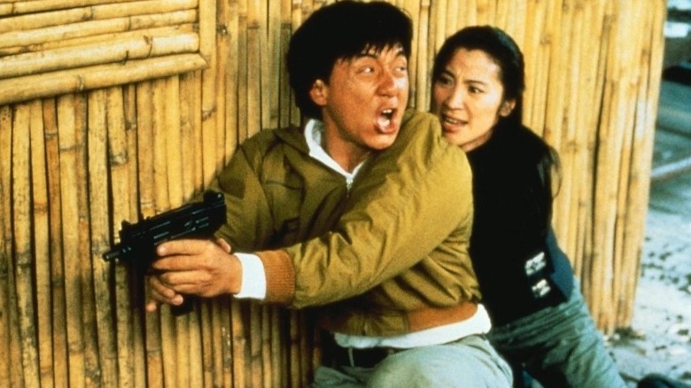 Jackie Chan with gun behind bamboo wall