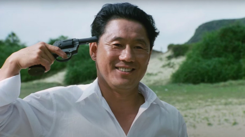 Takeshi Kitano holding gun to head, laughing