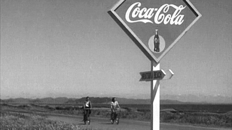 Late Spring Noriko rides by a Coca-Cola sign