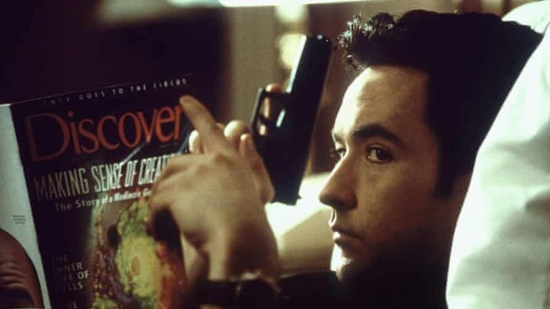 Cusack sits on couch with magazine and gun