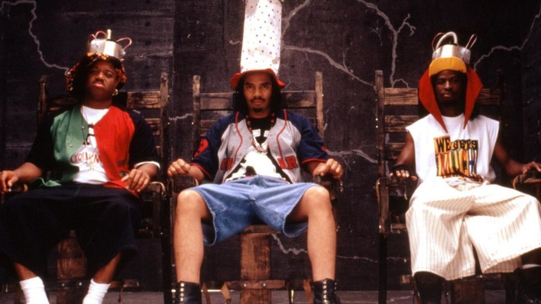 Three Black men sit on stage wearing giant ridiculous hats in Fear of a Black Hat.