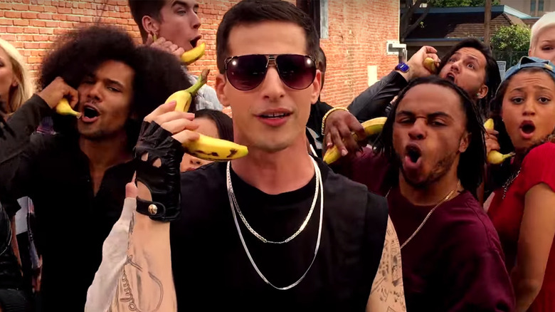 Andy Samberg holds a banana to his year like it's a phone.