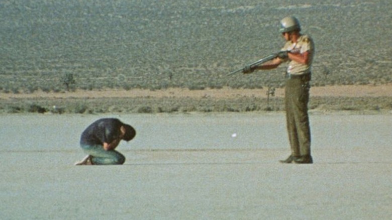 An officer points a gun at a person crouched on the ground in Punishment Park.