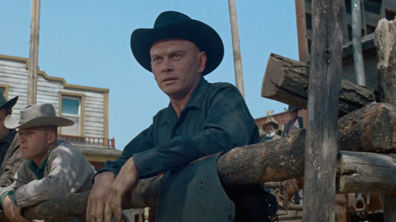 Yul Brynner as Chris Adams stands behind a fence in The Magnificent Seven