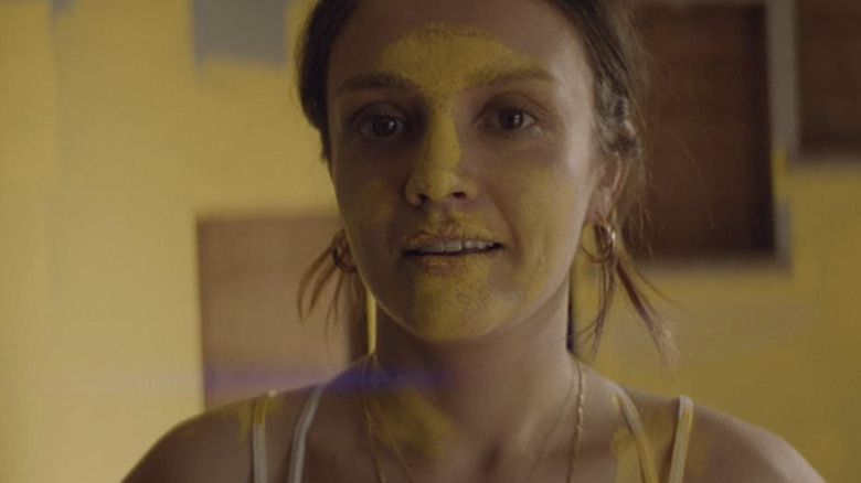 Emma staring with yellow paint smeared on her face and neck
